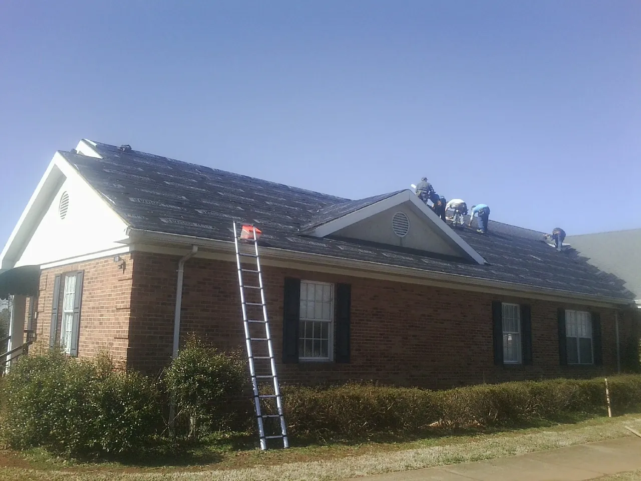 Crew tearing shingles off a brick ranch roof with a ladder set — Metal Roof Repair work by our crew in Pinole