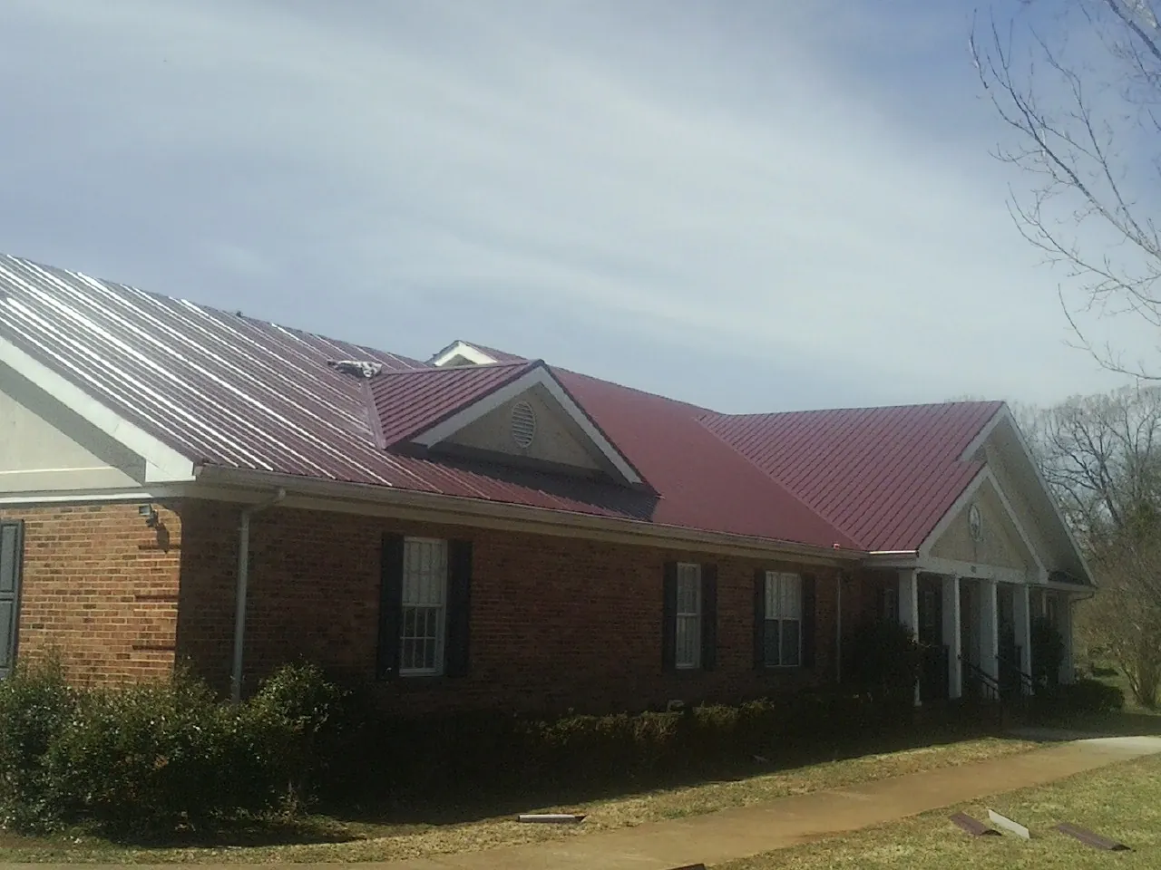 Red metal roof with gabled entries on a long brick building, from a Hail Damage Roof Repair job in Pinole