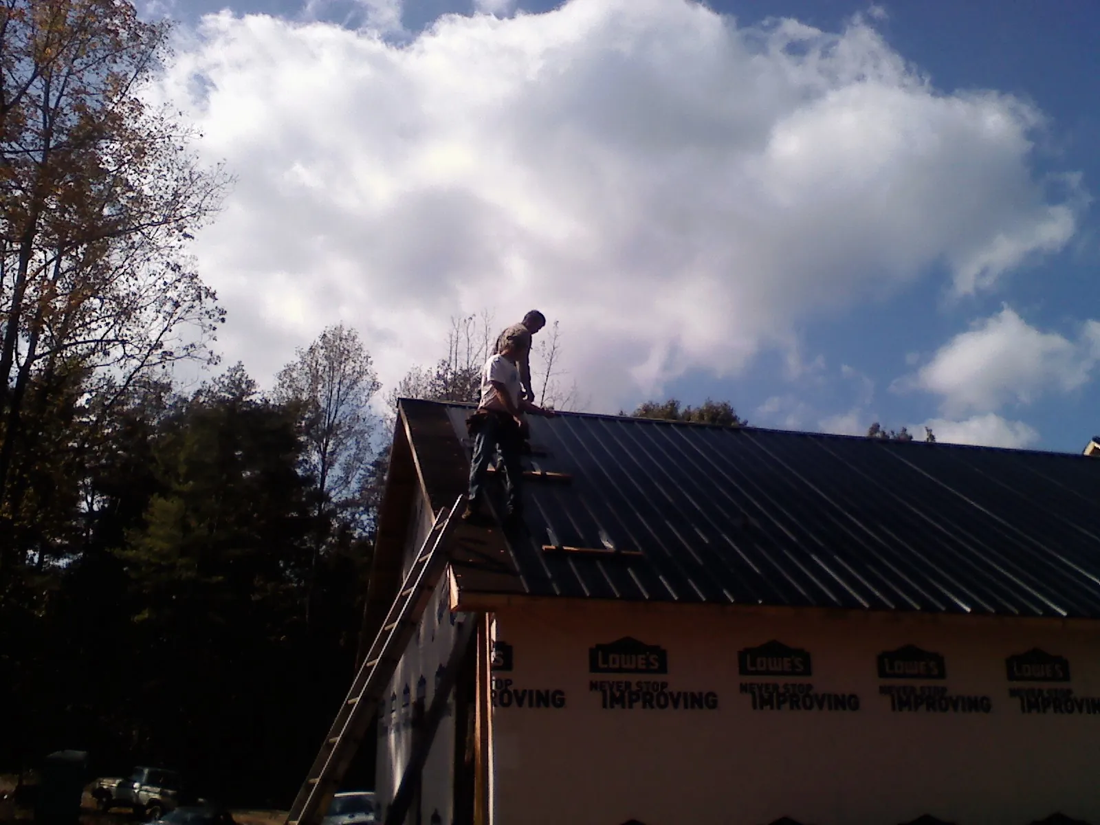 Roofer fastening dark metal panels high against a cloudy sky, from a Roof Inspection job in Pinole